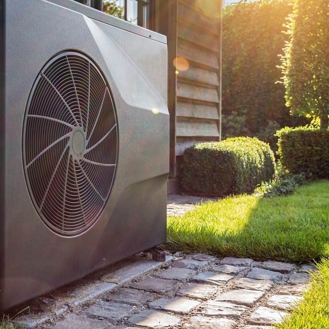 Pompe à chaleur air-eau : installation moderne en jardin Pompe à chaleur air-eau moderne grise avec ventilateur en spirale installée dans un jardin ensoleillé près d'un mur.